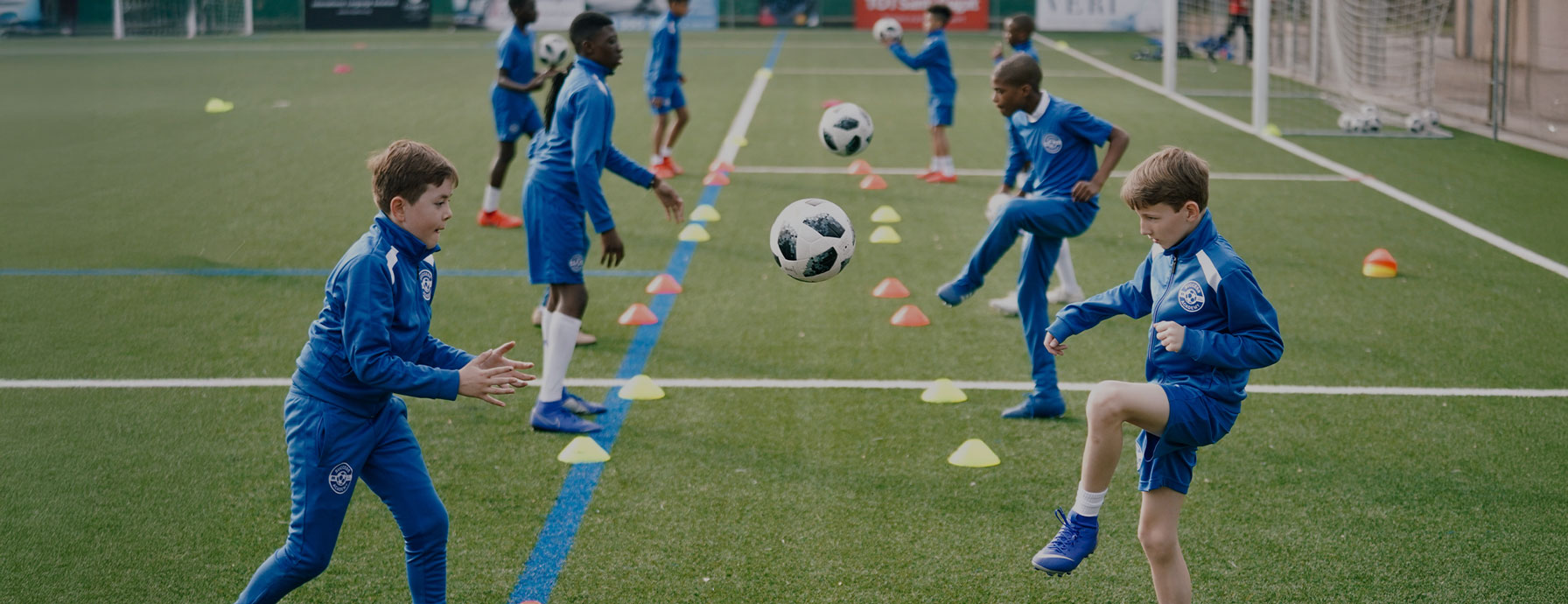 Success Academy elementary students play soccer in blue uniforms and practice on the field with soccer balls.