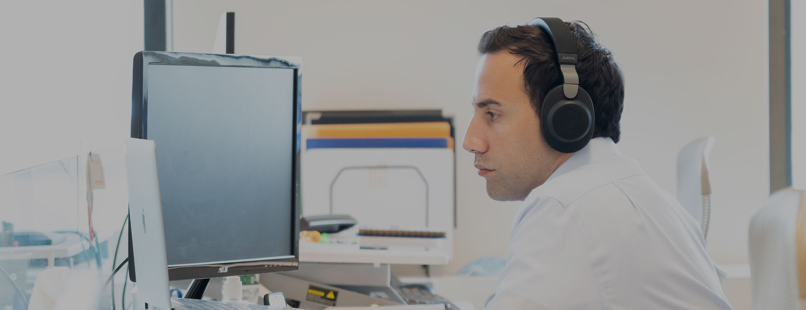A man wearing headphones looks intently at a computer monitor in the SA network office.