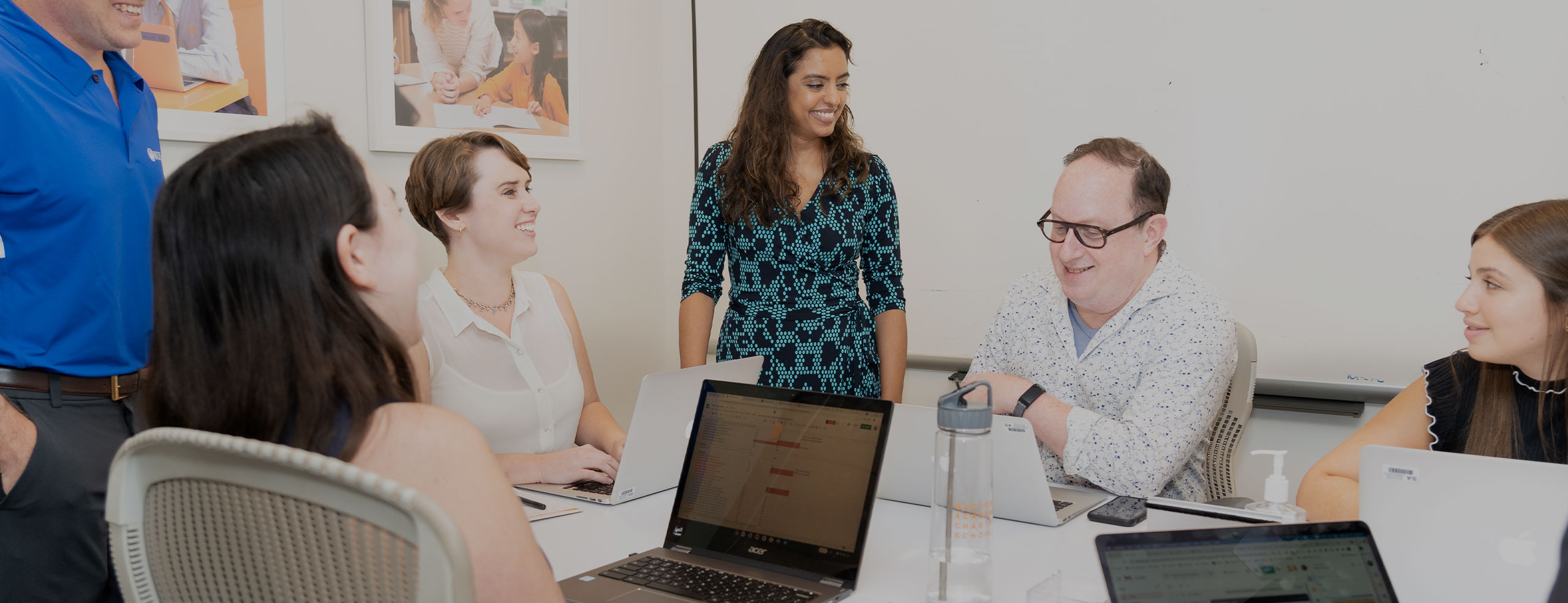 A diverse group of six professionals, including men and women, are gathered around a conference table in the SA network office, engaged in a meeting.
