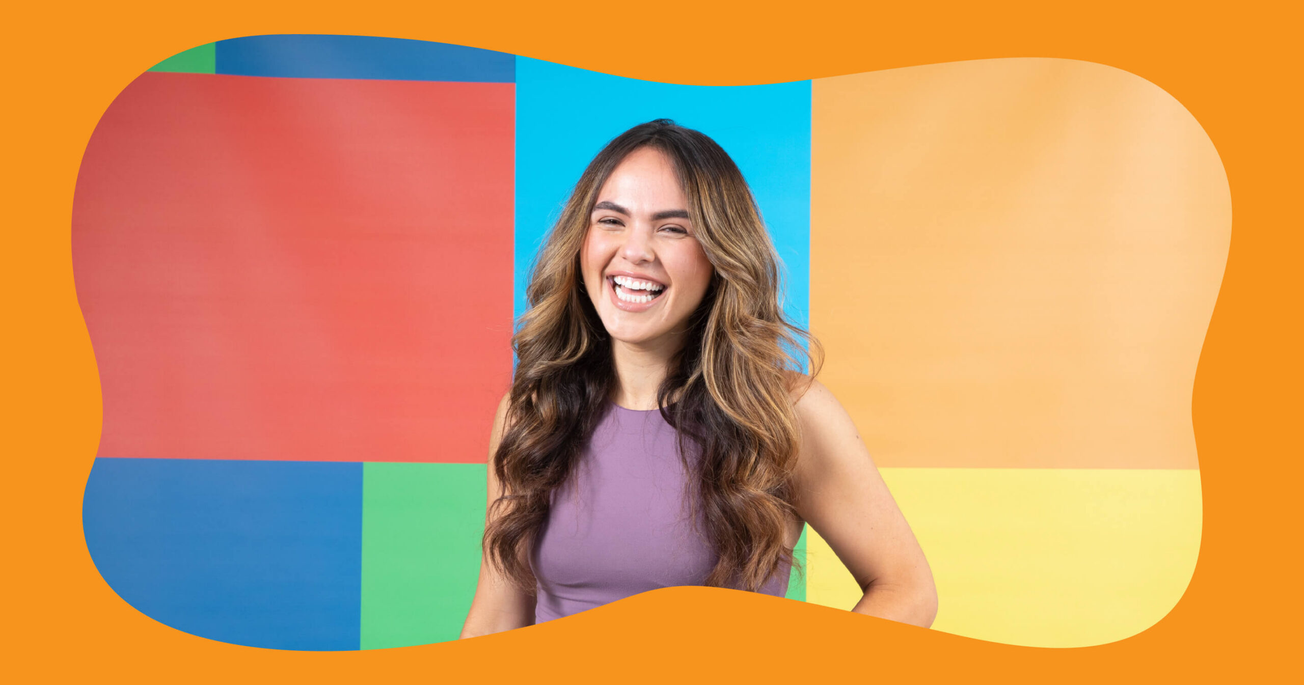 A cheerful SA employee with long, wavy brown hair, wearing a purple top, stands in front of a colorful background with blocks of red, blue, yellow, and orange. She is smiling broadly and looking at the camera. The entire image is framed by an orange, organic-shaped border.